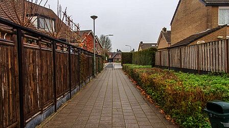 Een breed, losliggend voetpad door een woonwijk. Links van het pad zijn schuttingen, en rechts van het pad is een brede groenstrook met daarnaast schuttingen